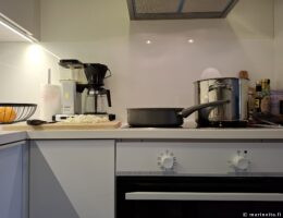 Liedellä keraaminen paistokasari ja teräskattila ja vieressä puinen leikkuulauta.