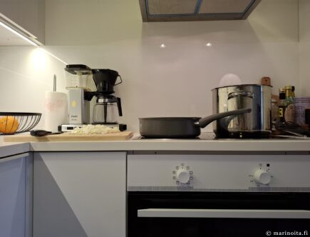 Liedellä keraaminen paistokasari ja teräskattila ja vieressä puinen leikkuulauta.